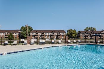 a lakeside pool with lounge chairs and apartments in the background at Bavarian Village Apartments, Indianapolis, IN, 46235
